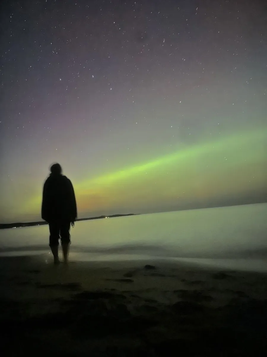 Person standing on the beach in front of the Northern Lights