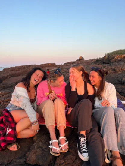 Four women sitting on a rock at sunset