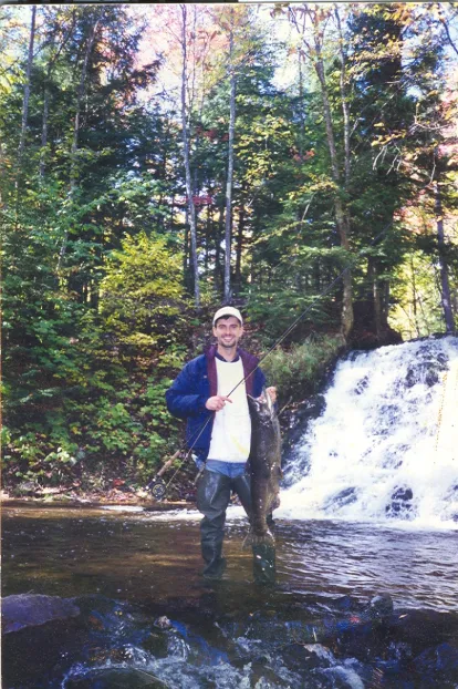Man holding fish in front of waterfall