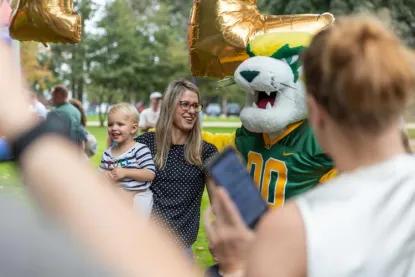 Wildcat Willy mascot posing with a women holding a toddler