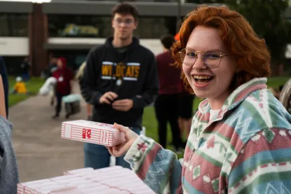 Student with red hair and glasses holding Popcorn box for outdoor movie on campus
