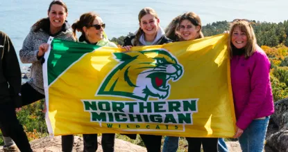 6 people standing on top of Sugarloaf Mountain holding a NMU flag