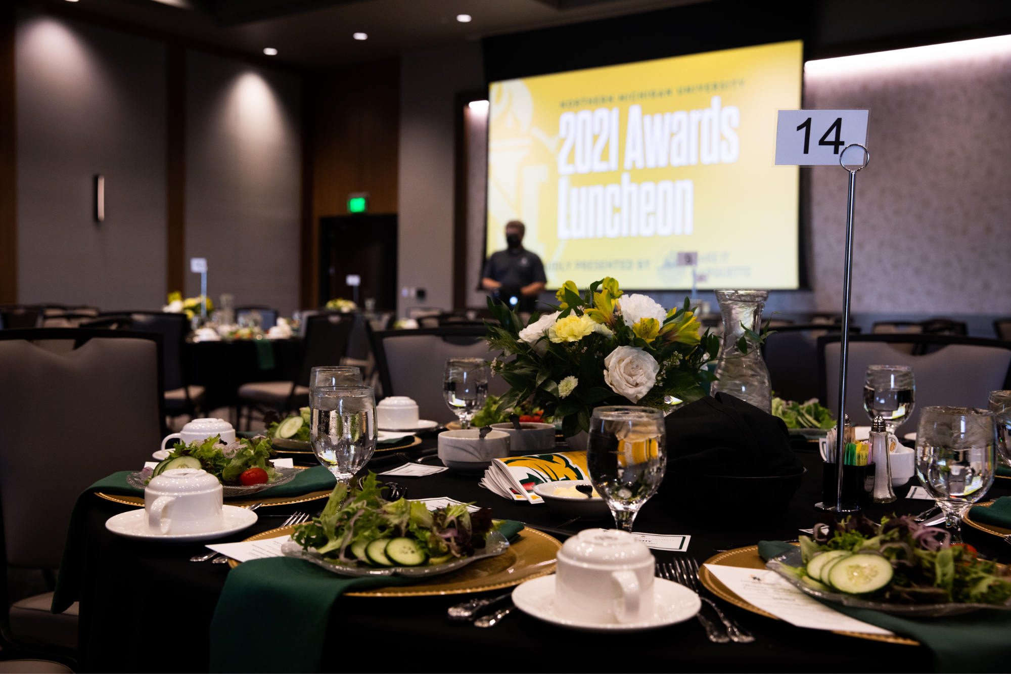 A table set for dinner with a presentation in the back reading "Alumni Awards Luncheon 2021"