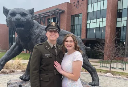 Garrett St. John in uniform with wife by Wildcat statue
