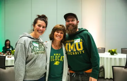 Three alumni in Northern Michigan University gear pose for a picture at the alumni reception