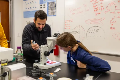 A professor and a student work together in a biology lab looking at cells under a microscope