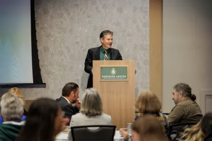 Man stands at Northern Michigan University branded podium addressing a crowd of faculty and staff
