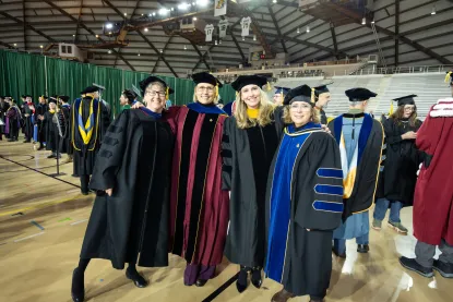 Four women dressed in faculty regalia post together at NMU commencement 