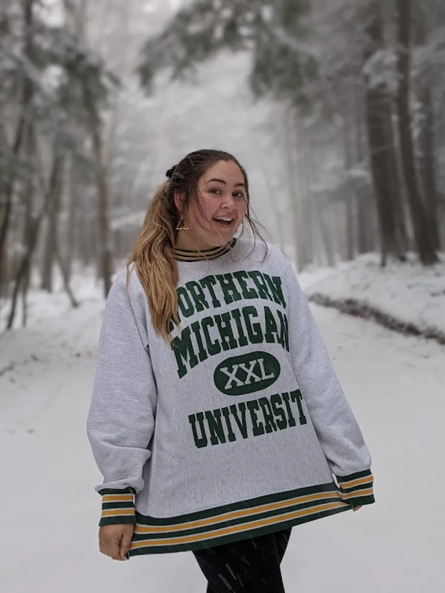Student standing in a snowy road, wearing Northern Michigan University Sweatshirt