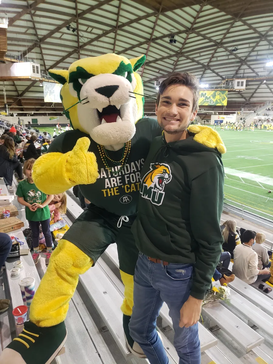 Student standing on metal bleachers next to Wildcat Willy mascot in the Superior Dome