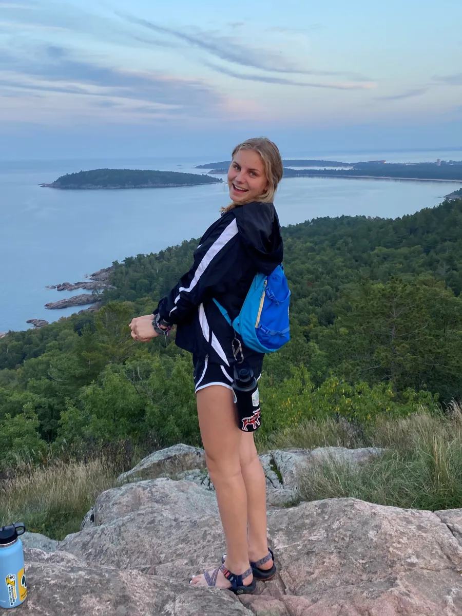 Student standing on a rocky outcropping with Lake Superior shoreline in the background. 