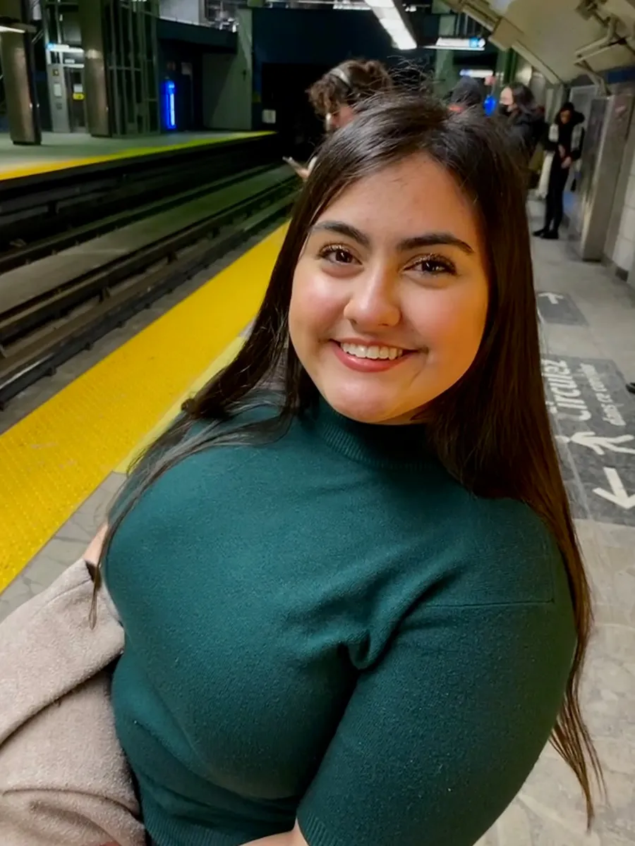 Student wearing green sweater standing in front of train tracks. 