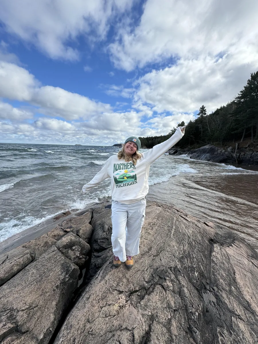 Ava standing outside gesturing widely at the surrounding wilderness