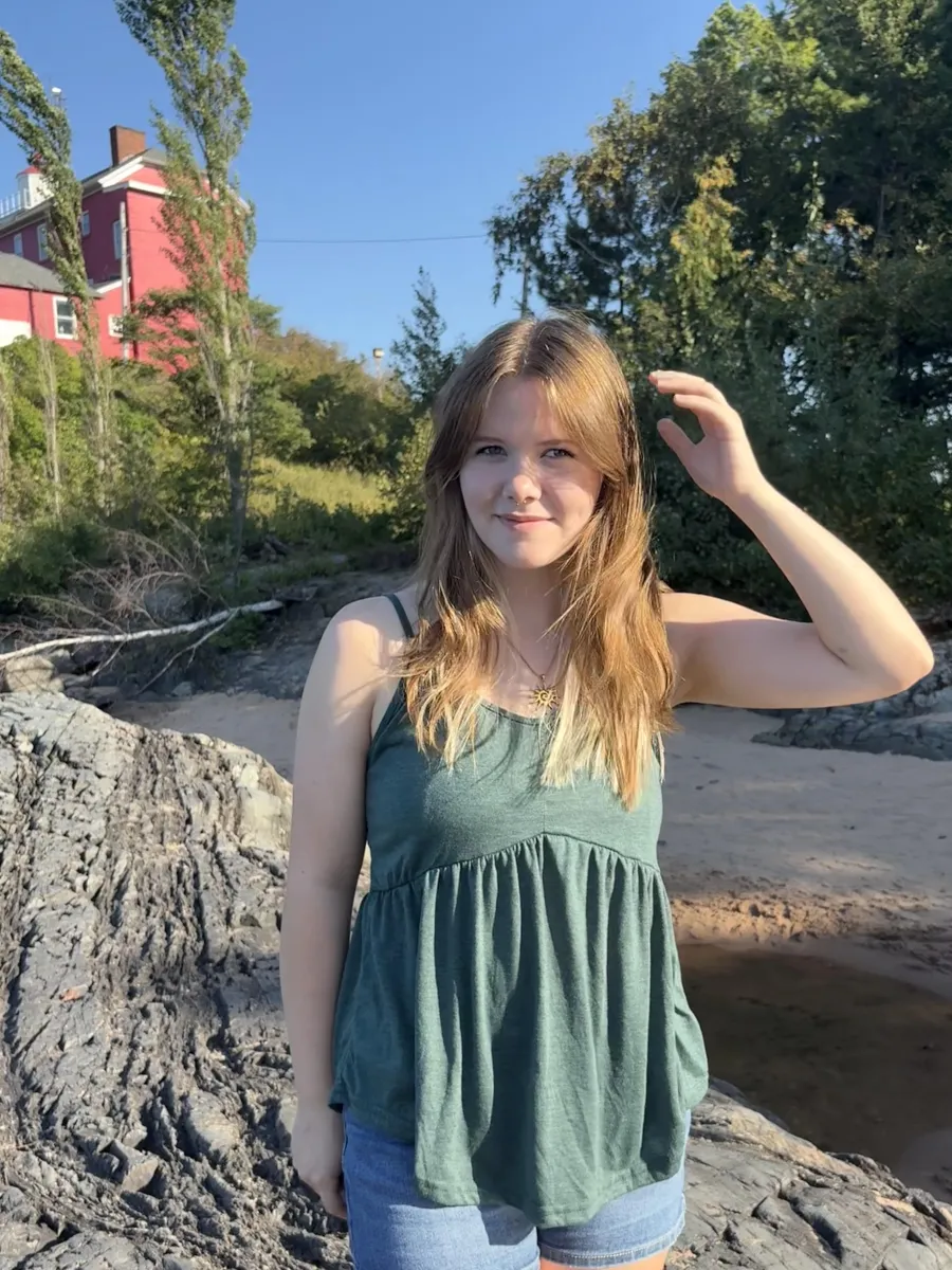 Keira standing on a beach by a lighthouse in summer