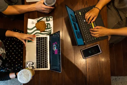 Overhead shot of a table with two laptops, students hands typing, and Starbucks treats.