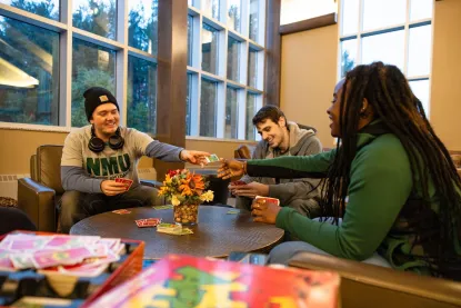 three college students playing a card game in a campus common area