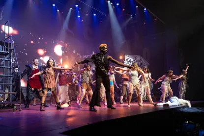 Theatre students performing an ensemble act on a dark stage with colorful lights