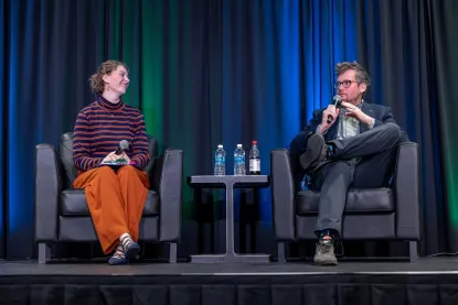 Author John Green sits on stage with a moderator while being interviewed.