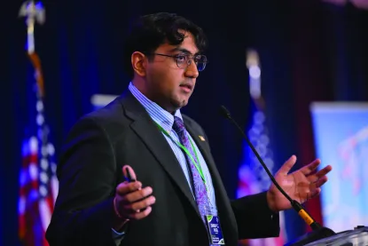A man stands at a podium speaking with the American flag in the background