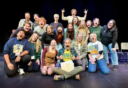 A group of theater students in a celebratory group photo on stage 