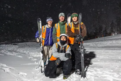 A group of four students with skis and orange vests post amongst a wintery scene