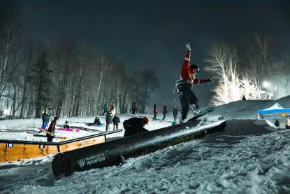 A snowboarder hitting a rail jump during a winter night at the ski hill.