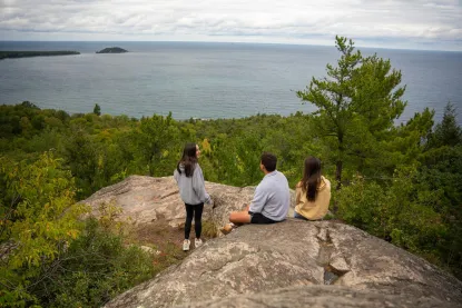 Three students sit on top of a mountain overlooking Lake Superior.