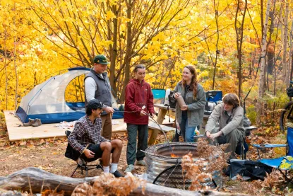 A group of students gather around a fire put at a campsite during the fall