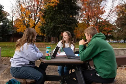 Three students sitting at a picnic table, talking.