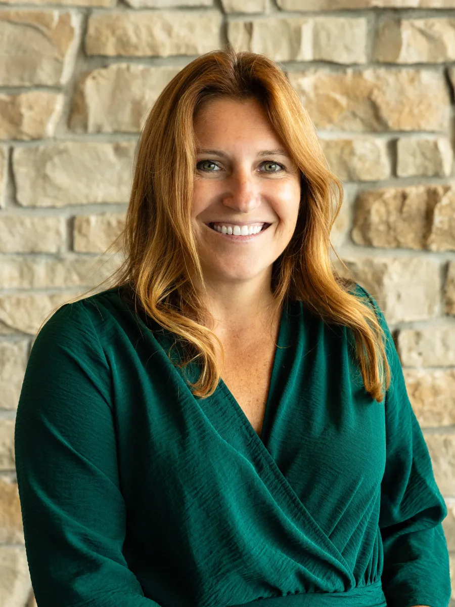 Headshot photo of a woman in a green blouse against a stone backdrop.