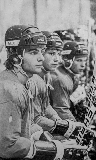 Three NMU hockey players in CCM helmets watch intently from the bench in this vintage black-and-white photo.