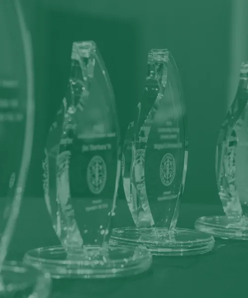 Five alumni awards on a table are showcased. A green filter is applied.