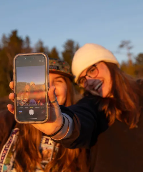 A girl holding a phone smiles for a selfie with her friend