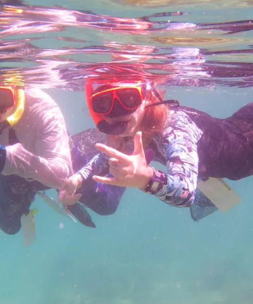 View of two students looking at the camera from underwater. Wearing snorkels and masks. 
