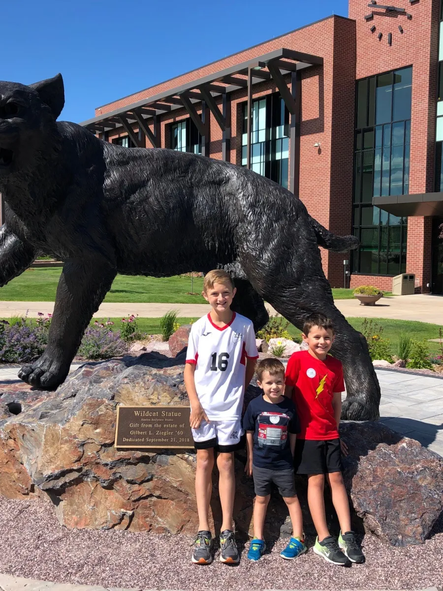 Three kids standing in front of the wildcat statue