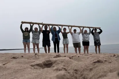 Eight students lifting a log on a beach