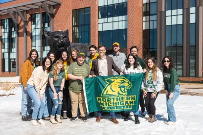 Several students and NMU's president pose for a picture with an NMU flag