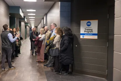 	 A group of adults stands in a hallway, listening to a person speaking. 