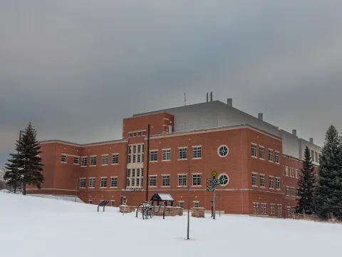 Weston is a large brick building behind a snow-covered campus, with evergreen trees and bicycles under a gray winter sky.