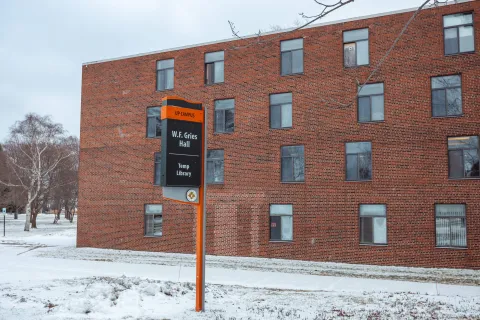 Gries Hall is a four-story red brick building with rows of rectangular windows. Snow covers the surrounding ground and sidewalks.