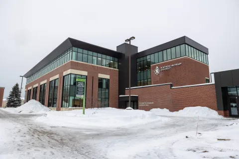 Elizabeth and Edgar Harden Hall, is a red brick building with large glass windows, dark metal paneling. Snow covers the surrounding walkways and landscaped grounds.