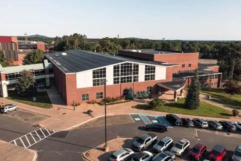 An aerial view of Hedgcock, a red brick building with large window A parking lot with accessible parking spaces and surrounding trees and walkways sits in front of the building.