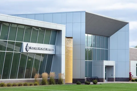 A modern building with angled glass windows, blue-gray metal panels, and a yellow brick column.