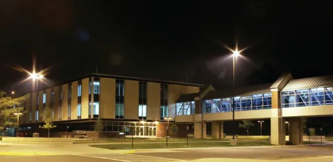 Modern glass-and-brick academic building illuminated by streetlights.