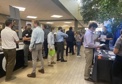 Multiple employer tables and many professionally-dressed students talking to employers at the Construction Management & Technology Career Fair in 2021