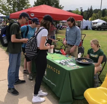 Three students looking at the Career Services table at Fall Fest in 2021, with Grant Langdon and a student employee on the other side of the table