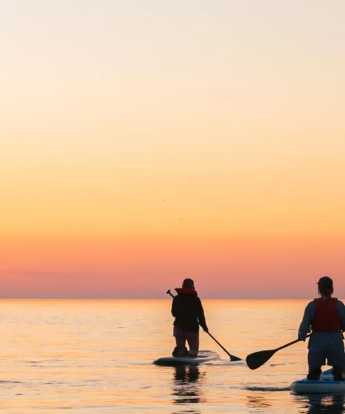 Two students paddleboarding at sunrise on lake superior