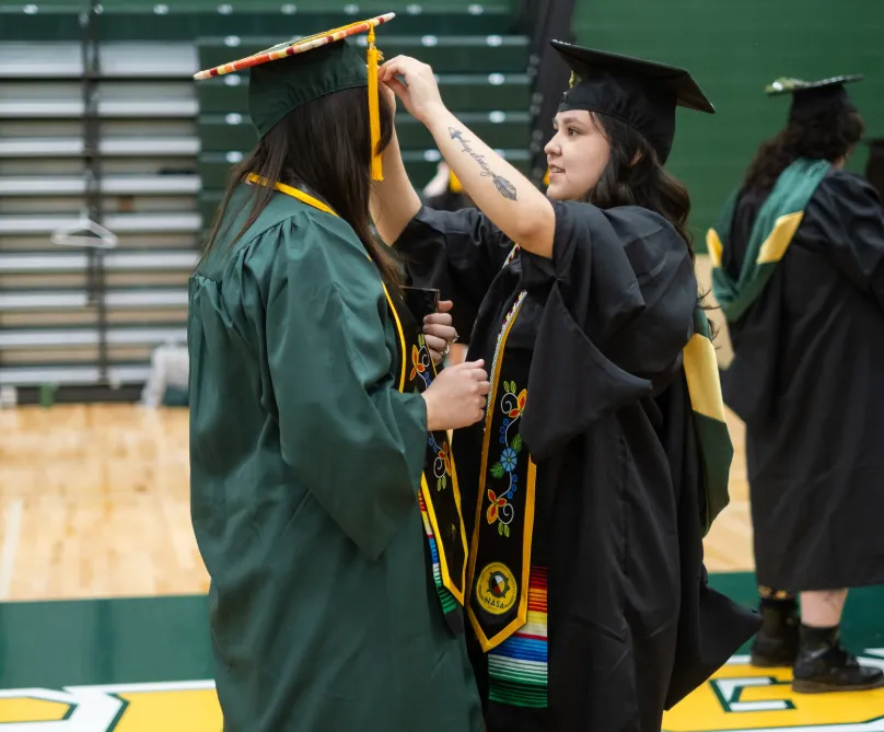 Student helping adjust another graduate's Cap before Commencement