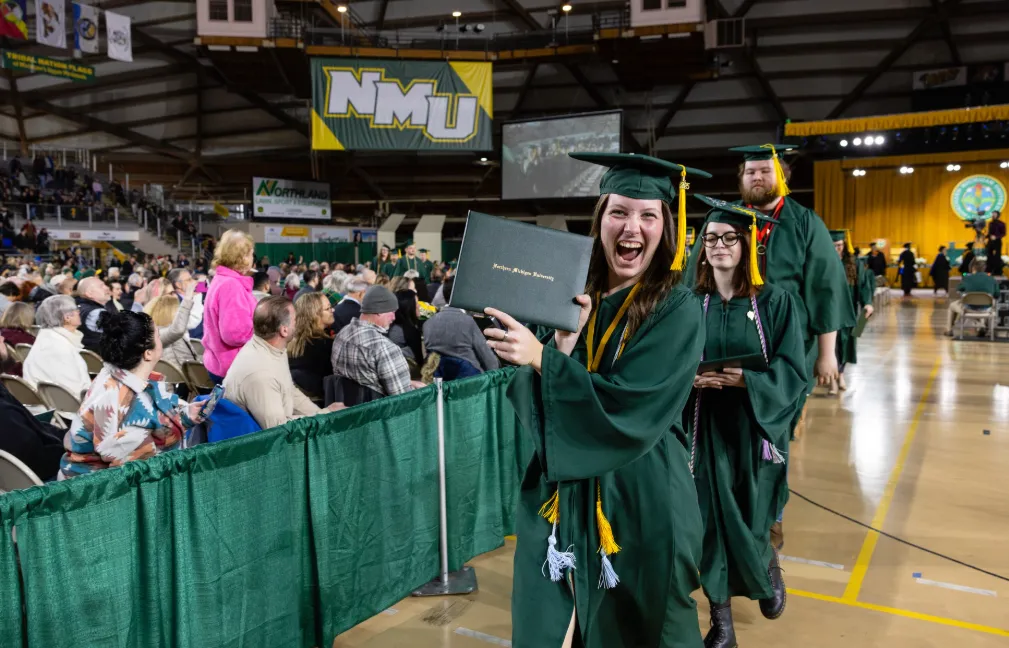Student holding up their diploma cover while leaving commencement