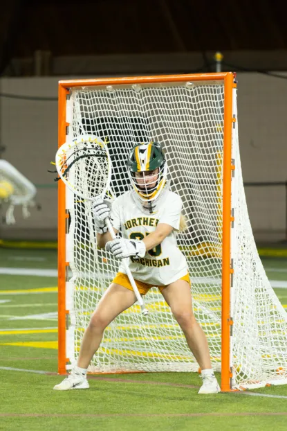 An image of a young lacross goalie in NMU green and Gold